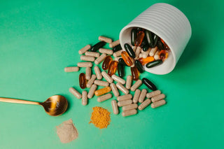 Assorted multivitamin capsules and softgels spilled from a white container on a green surface, representing daily multivitamin supplements in Singapore.